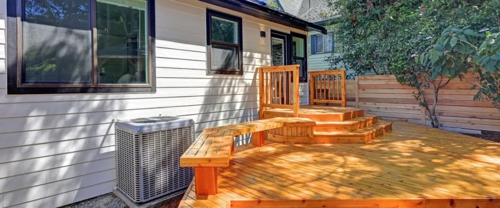 A high-angle shot of a newly stained cedar wood backyard deck featuring a multi-level design with wide stairs, built-in bench seating, and a horizontal wood privacy fence in the background.
