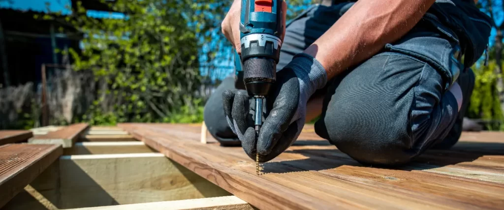 a person using a cordless drill to install wooden decking outdoors