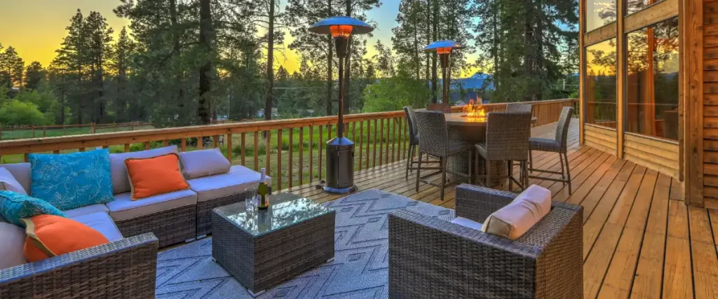 an outdoor wooden deck attached to a house, furnished as an inviting living and dining area in a scenic, forested location at sunset