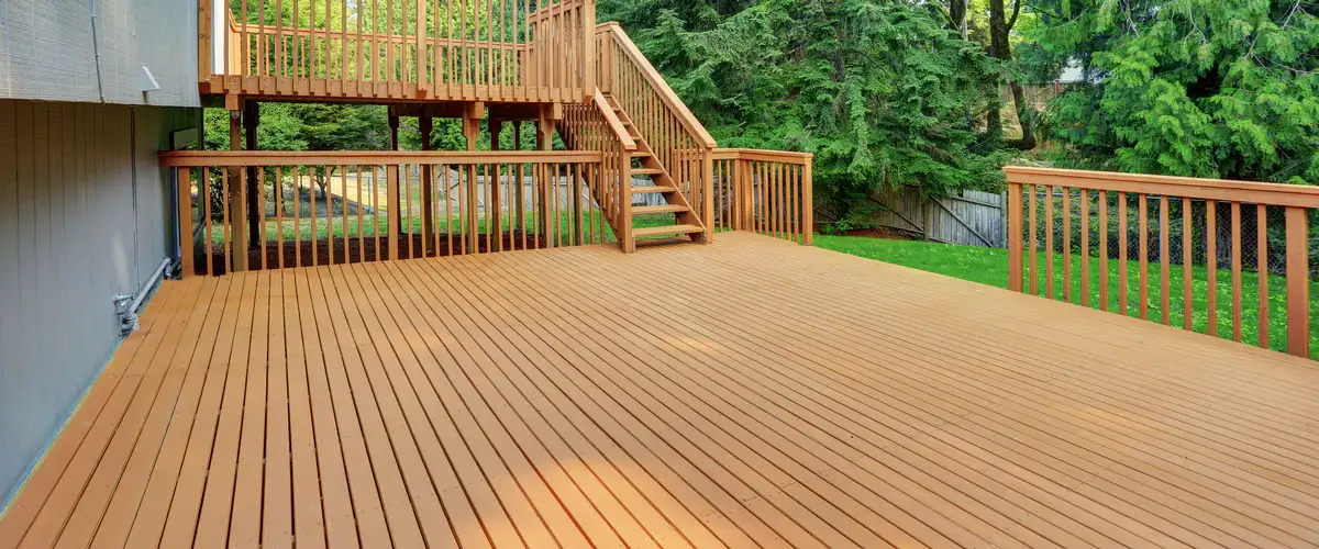 A spacious multi-level wooden deck with a built-in staircase and matching brown wood railings attached to a residential home.