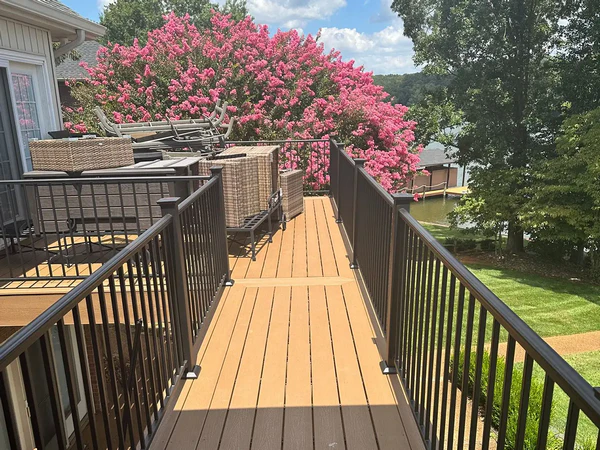 A high-quality composite deck replacement in Vonore, TN, by Riverview Decks, featuring tan decking boards, sleek black aluminum railings, and a scenic lakefront view with blooming pink Crepe Myrtle trees in the background.