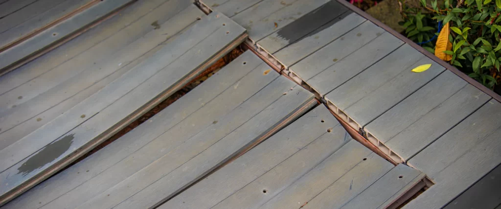 Top-down view of a warped deck featuring grey composite boards that are unevenly spaced and buckling at the joints.
