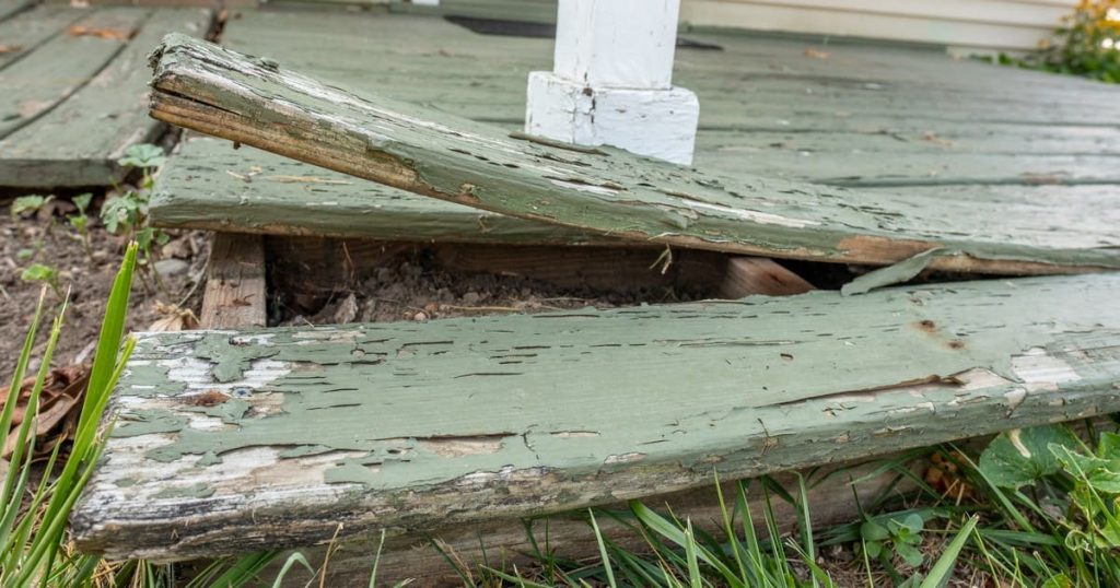 A close-up of severely warped and peeling green wooden deck boards lifting away from the frame, illustrating why some decks warp more than others.