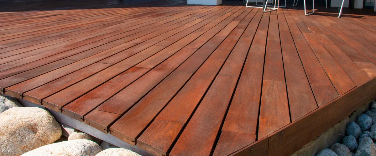 A detailed close-up of dark-stained wooden deck planks meeting a landscaped border of large, light-colored river rocks.