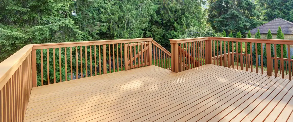 A large, newly constructed wooden deck featuring a built-in safety gate, wrap-around railings, and stairs overlooking a lush evergreen forest.