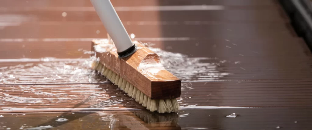 A homeowner performing deck maintenance by applying a protective waterproof sealant to wooden boards.