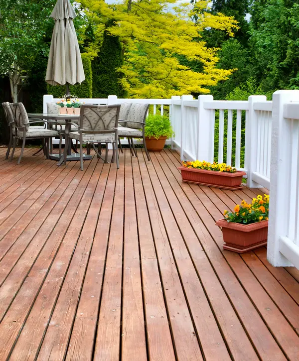 A beautiful deck replacement in Chattanooga, TN featuring redwood-stained planks, contrasting white railings, and a patio dining set with yellow flowers.