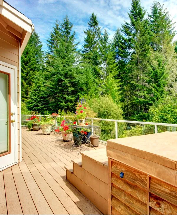 A scenic multi-level wooden deck featuring a covered hot tub, glass railings, and vibrant potted flowers, highlighting expert deck repair in Chattanooga, TN.