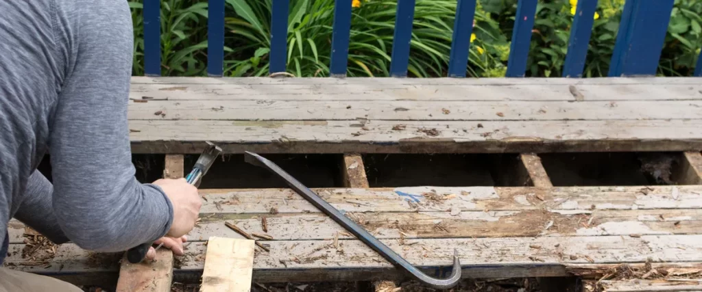 A technician performing deck fixing on a weathered outdoor timber patio.
