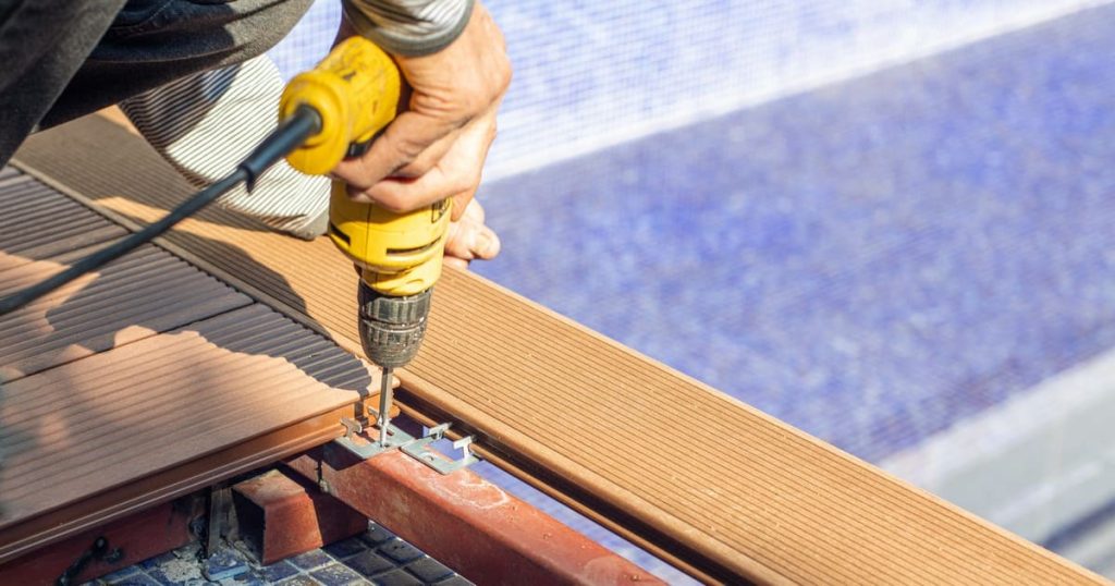 Close-up of a worker fixing wooden deck planks using professional tools.