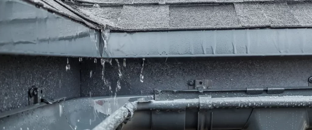 Rainwater pouring from a house roof directly onto a deck due to overflowing or missing gutters.