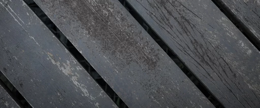 Detailed view of a water-damaged deck featuring graying wood, mold growth, and structural rot from moisture.