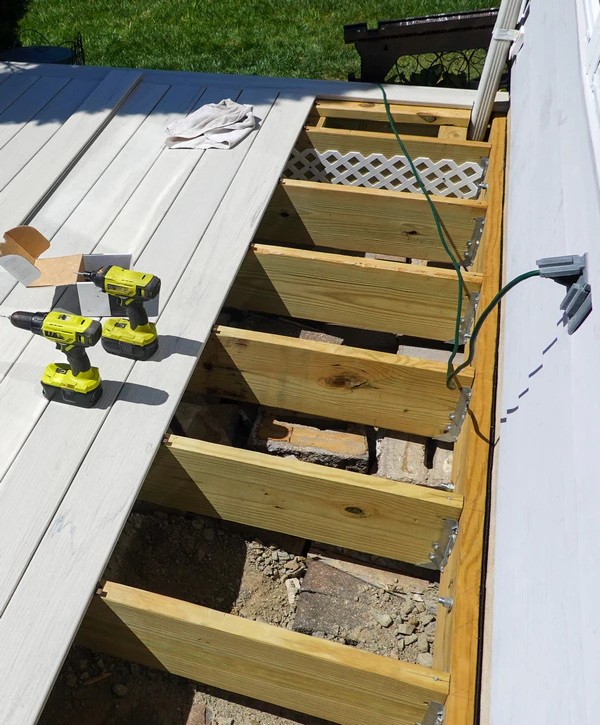 A partially completed deck showing composite boards laid over wooden joists attached to a house via metal hangers during a deck ledger installation project in Knoxville, TN. Two yellow power drills rest on the finished surface.