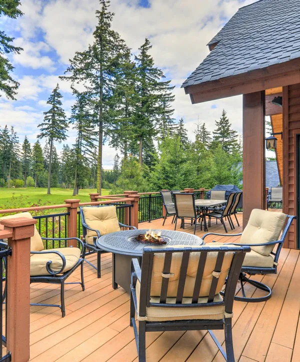 Cushioned lounge chairs arranged around a round metal fire pit table on a raised wooden deck overlooking pine trees, showcasing completed deck furniture assembly in Knoxville, TN.