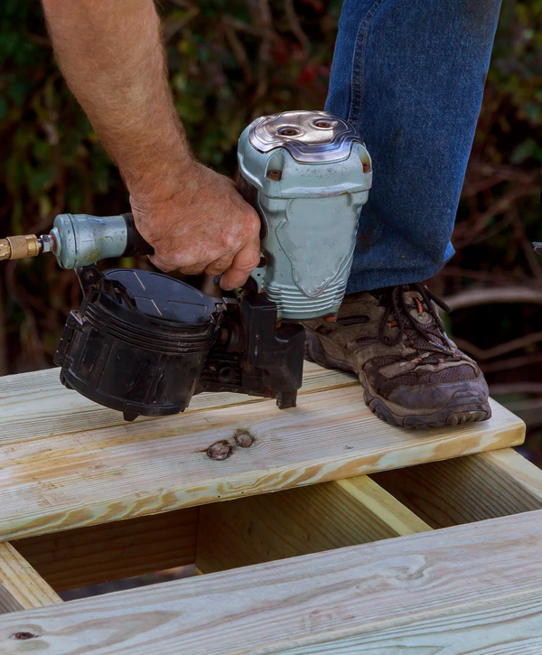 A close-up of a worker using a pneumatic nail gun to fasten fresh wooden boards during a deck repair in Amherst, Knoxville, TN.