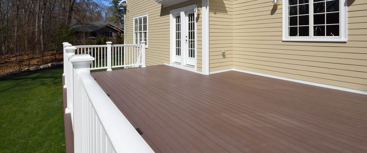 A spacious, newly finished dark brown deck featuring bright white railings attached to the back of a house with yellow siding.
