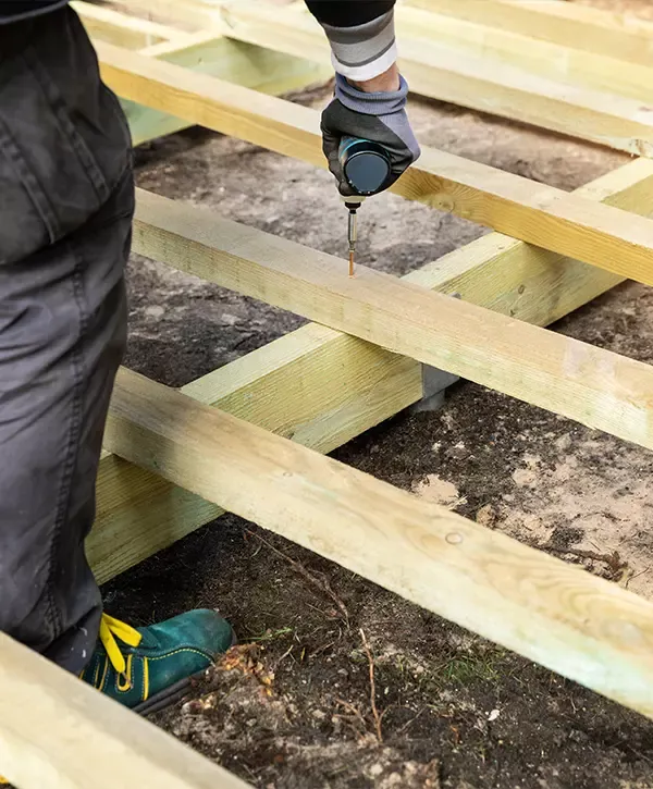 A contractor wearing gloves uses a power drill on the wooden frame joists during a Deck Repair in Woodland Acres, Knoxville.