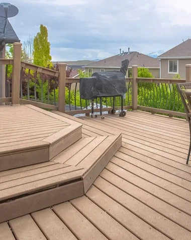 Multi-level composite deck featuring a step-down platform, a covered grill, and a woven patio dining set overlooking a suburban neighborhood, showcasing professional deck building in Concord, TN.