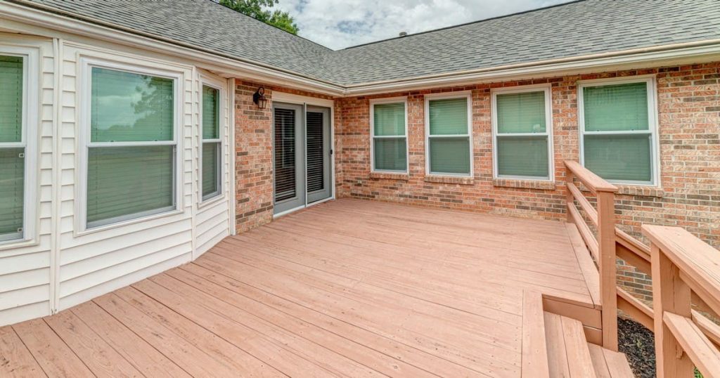 A clean, freshly finished wooden redecking surface attached to a classic red brick house with white-trimmed windows and double glass patio doors.