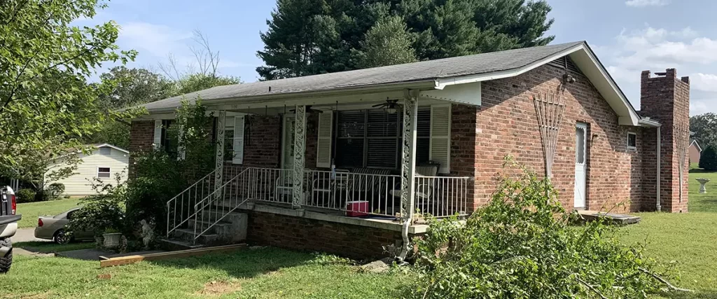 Brick ranch home exterior before deck addition with covered porch and large backyard