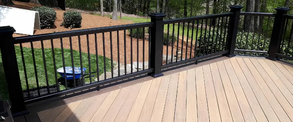 Composite deck with black aluminum railing overlooking landscaped backyard and wooded area