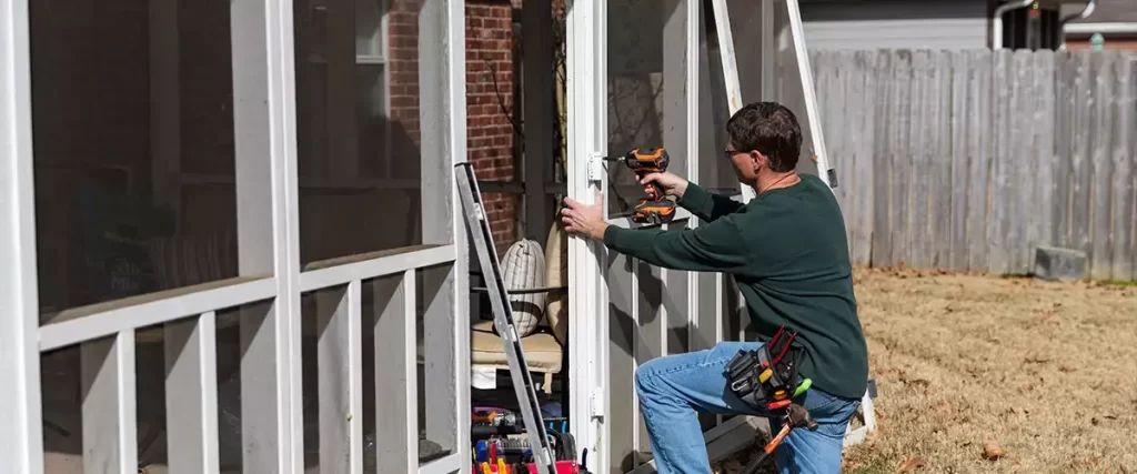 Contractor installing screened porch panels on custom outdoor living addition with power drill