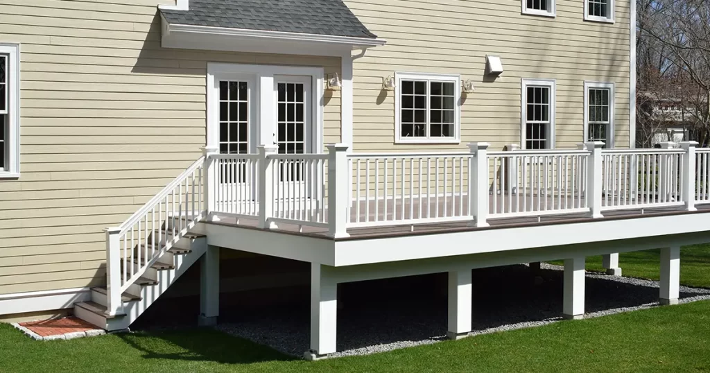 Elevated backyard deck installation with white railing and stairs on a custom home exterior