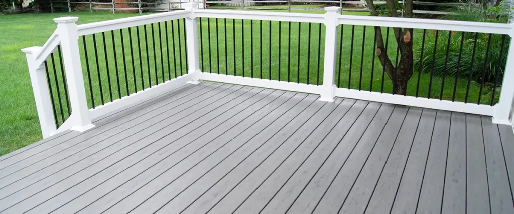 Gray composite deck with white railing and black balusters in a spacious backyard setting