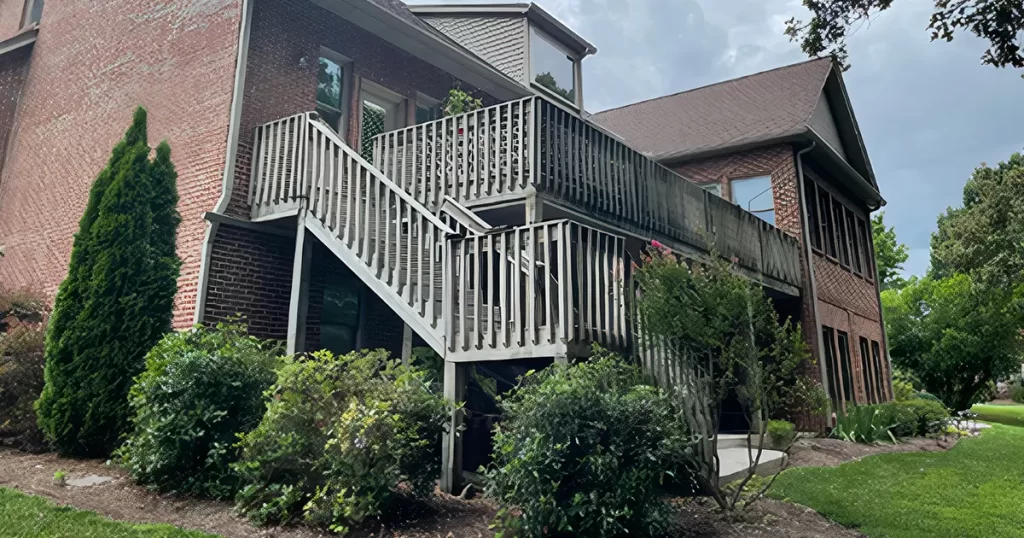 Multi-level wood deck with stair railing attached to large brick home and landscaped backyard
