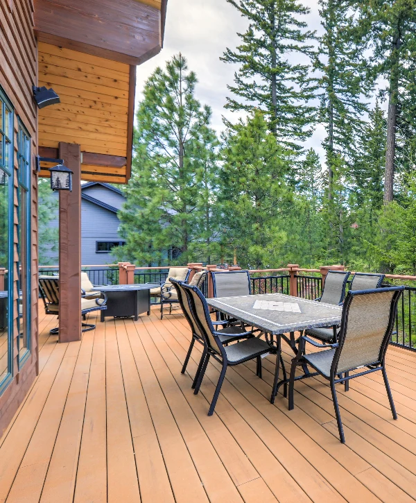 An elevated outdoor living space featuring a dining table, fire pit area, and black metal railings, highlighting premium deck building surrounded by pine trees in Wood Creek West, Knoxville, TN.