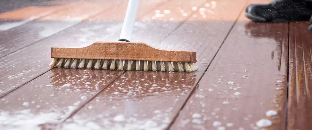 Detail of a scrubbing brush during spring cleaning on a wooden terrace with soap and splashes of water